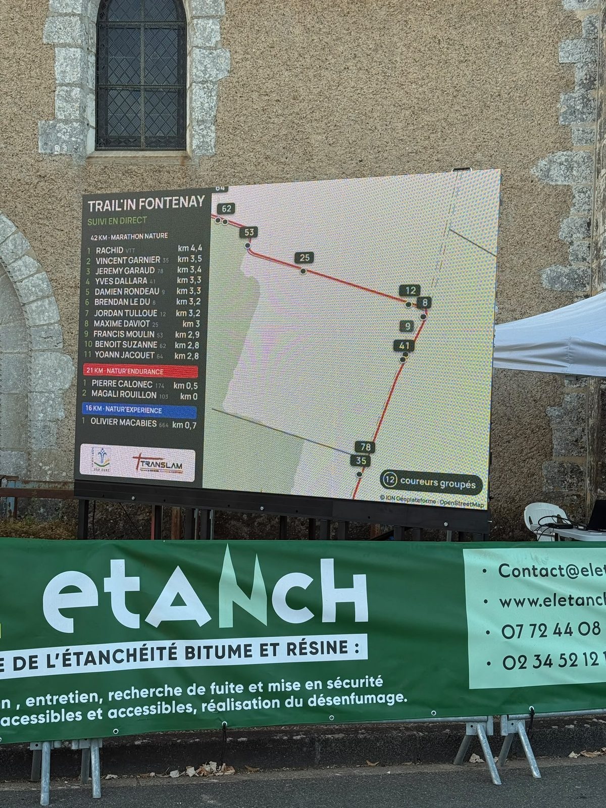 Écran LED de 3 × 2 m allumé sur la place de Fontenay-sur-Eure, près de l'église, pendant le trail